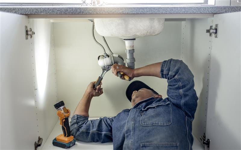Plumber repairing pipes beneath a bathroom sink in Newport Beach